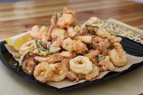 Un piatto invitante di frittura di pesce croccante, con gamberi, anelli di calamaro e verdure, accompagnato da uno spicchio di limone.