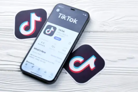 Telefon z aplikacją TikTok i logotypy platformy. Zastanawiasz się, ile zarabia się na tiktoku za 1000 wyświetleń?