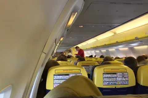 Wnętrze samolotu Ryanair, pasażerowie siedzą w rzędach. Na oparciach siedzeń widoczne są żółte tabliczki z instrukcjami bezpieczeństwa, co może uspokoić osoby zastanawiające się, czy Ryanair jest bezpieczny.