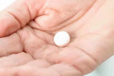 Dłoń trzyma białą tabletkę, być może Vicodin, która ma sfinansować ulgę w bólu.