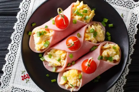 Roladki z szynki z jajecznicą i szczypiorkiem, ozdobione pomidorkami koktajlowymi.