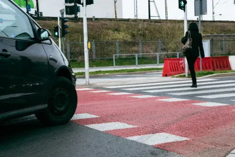 Kobieta przechodzi przez pasy, stosując się do zasady prawej ręki, gdy zielone światło dla pieszych pozwala na ruch.