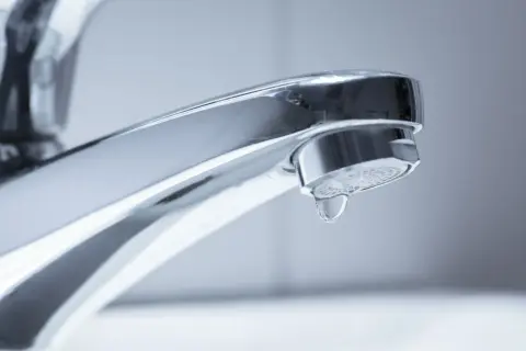Ein glänzender Chrom-Wasserhahn, bei dem ein einzelner Tropfen Wasser langsam herunterfällt. Der Wasserhahn tropft.