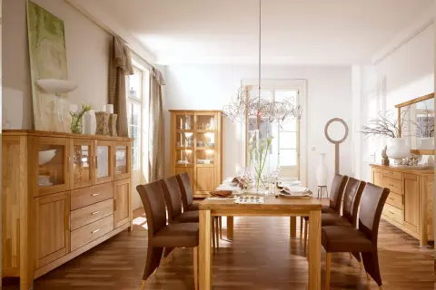 Nowoczesny salon ze starymi meblami z litego drewna. Dębowe komody i witryny tworzą ciepłą atmosferę, a skórzane krzesła przy drewnianym stole zapraszają do wspólnego posiłku.