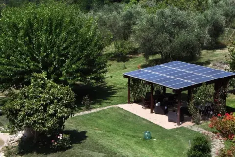 Un pergolato con pannelli fotovoltaici a terra in giardino, in linea con la normativa, offre ombra e energia pulita.