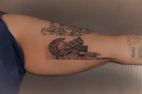 Tatuaż mikrorealizm przedstawiający antyczne hełmy i twarze, zlewające się w abstrakcyjny wzór.