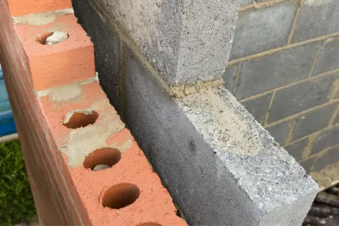 Dettaglio di una parete in costruzione con mattoni rossi forati e blocchi di cemento grigio. Si intravede lo spazio vuoto tra le due murature, ideale per l'**insufflaggio pareti**.