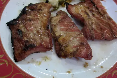 Tres trozos de secreto ibérico al horno, jugosos y con sal gruesa, servidos en un plato blanco con borde rojo.