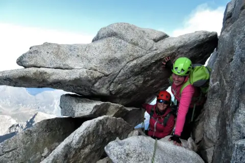 Zwei Bergsteigerinnen auf dem Olperer Nordgrat, lächelnd unter einem Felsvorsprung.