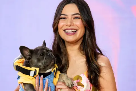 Miranda Cosgrove lächelt und hält einen französischen Bulldoggen-Welpen in einem gelben Outfit. Vielleicht ein neuer Co-Star für ihre Filme?