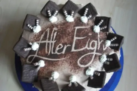 Eine After Eight Torte mit Schokoladenquadraten und Sahnetuffs. Der Schriftzug "After Eight" ist in Kakao auf die Torte gestreut.