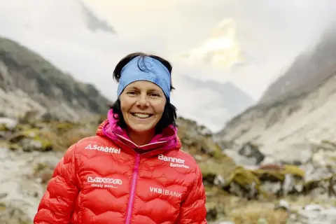 Kristin Harila, bereit für den K2, lächelt in die Kamera, umgeben von majestätischen Bergen.