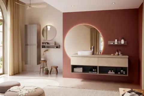 Salle de bain moderne avec murs rose terre et beige, meuble vasque en bois clair, miroir rond lumineux. La couleur salle de bain est chaleureuse et apaisante.
