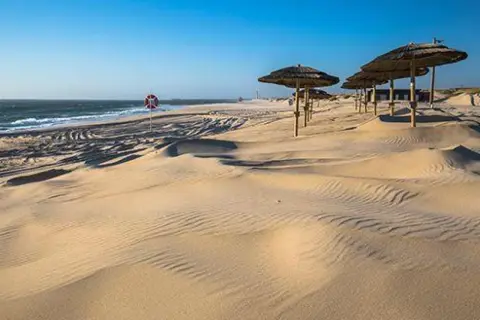 Dunas de arena dorada con sombrillas de paja y un salvavidas, un oasis de paz que recuerda a las playas cerca de Salamanca.