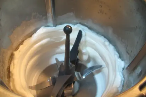 Batidora procesando claras a punto de nieve, creando una textura esponjosa y blanca, lista para un postre.