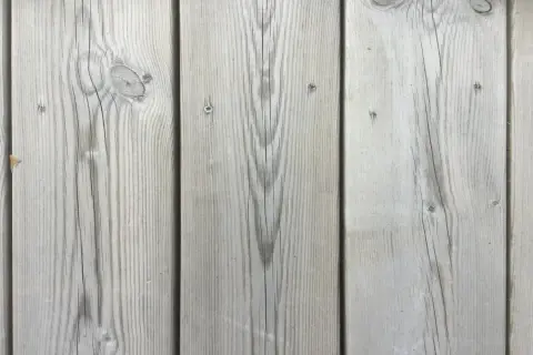 Grå träplankor med synliga kvistar och ådring, som en kisel altan i sommarsolen.