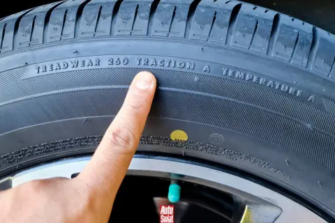Palec wskazuje żółtą kropkę na oponie, obok napisu "TRACTION A".