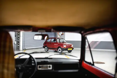 Widok z wnętrza samochodu na lśniącego, **fiat 126p elegant** w kolorze wiśniowym, stojącego w garażu.