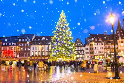 Magiczny, ośnieżony wieczór na jarmarkach bożonarodzeniowych w Europie. Rozświetlona choinka i tłumy ludzi tworzą świąteczną atmosferę.