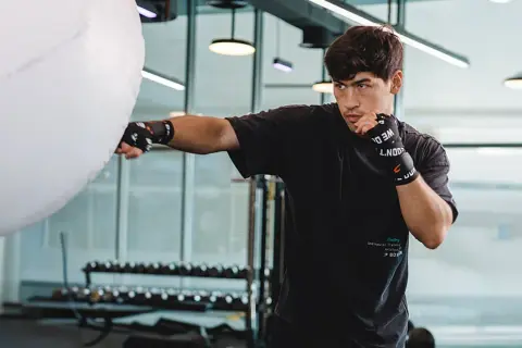 A young man practices Russian boxing, throwing a punch at a large white training bag in a modern gym.
