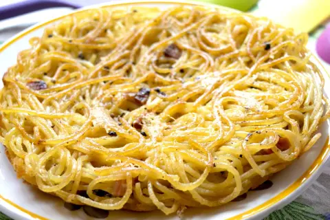 Una dorata frittata di scammaro, con spaghetti croccanti e pezzetti di pancetta, pronta per essere gustata.
