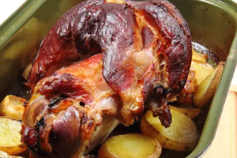Pieczona golonka z ziemniakami w zielonej brytfannie.