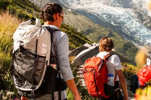 Zwei Wanderer mit Rucksäcken auf einem Bergpfad. Die Frage "was zieht man zum wandern an" wird durch ihre funktionale Kleidung beantwortet.