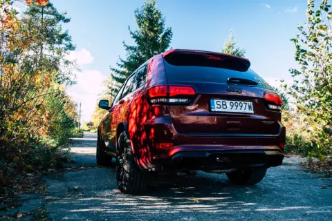 Ciemnoczerwony Jeep Grand Cherokee Trackhawk na tle jesiennego krajobrazu.