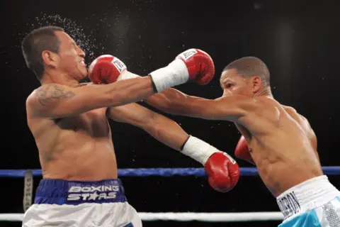Two boxers in the minimum weight category exchange blows in a tense match. One fighter recoils as a punch lands, sending sweat flying.