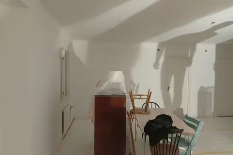 Rummet är nymålat vitt, möbler är täckta med plast. Skuggor på väggarna antyder att det är en pågående renovering, vilket väcker frågan: hur lång tid tar det att måla ett rum?
