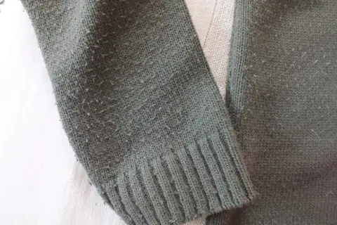 Zielony sweter z dzianiny, na którym widać, czy bawełna się kulkuje. Włókna tworzą drobne kuleczki na powierzchni materiału.