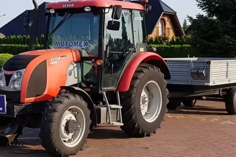 Czerwony Zetor z przyczepą, gotowy do pracy. Posiadanie prawa jazdy na traktor otwiera drogę do takich maszyn.