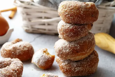 Gestapelte, zuckerglasierte Apfelkrapfen aus dem Airfryer, daneben weitere Krapfen und ein Ei.