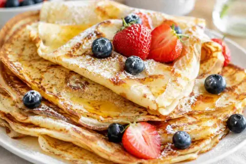 Ein Stapel goldbrauner Pfannkuchen, bestäubt mit Puderzucker und garniert mit frischen Beeren und Honig. Ein einfaches Pfannkuchen-Rezept, das jeden Tag zum Genuss macht.
