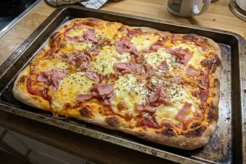 En nygräddad pizza med rikligt med smält mozzarella och skinka, redo att avnjutas.