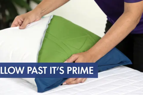Hands adjust a pillow, hinting at how often should you change your pillows on your bed.