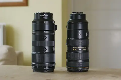 Two Nikon telephoto lenses, including a Nikkor 200mm f2, stand side-by-side on a wooden table.