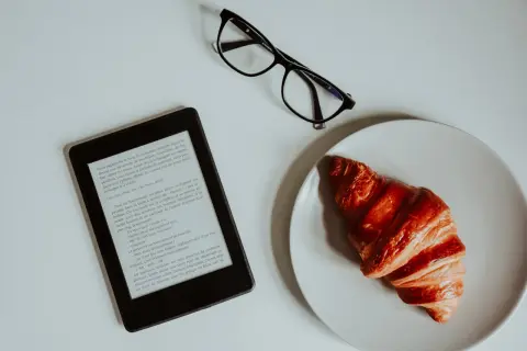 Un e-reader, des lunettes et un croissant sur une assiette. Idéal pour créer un epub et s'évader dans une histoire.