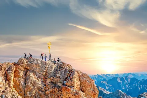 Menschen auf dem Gipfel der Zugspitze mit goldenem Kreuz. Die Zugspitze Aufstieg Dauer ist lang, aber die Aussicht ist es wert.