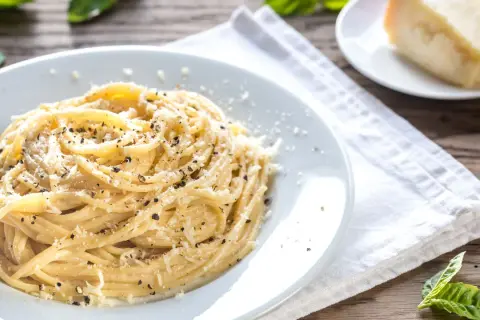 Un piatto di spaghetti fumanti conditi con abbondante cacio e pepe, guarniti con pecorino grattugiato e pepe nero macinato fresco.