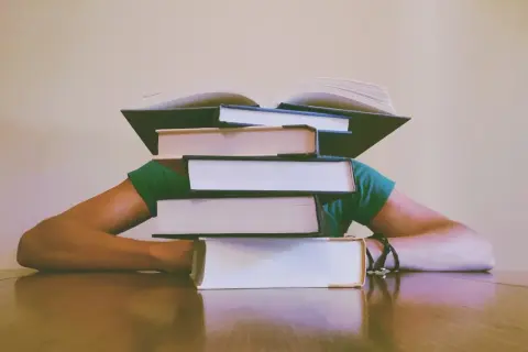 Stos książek przygniata głowę studenta. Jak napisać dyskusję w pracy magisterskiej? Czas na naukę!