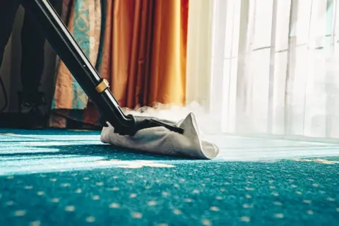 Dampfreiniger reinigt einen blauen Teppich mit Muster. Dampf steigt auf, während die Düse über den Boden gleitet.