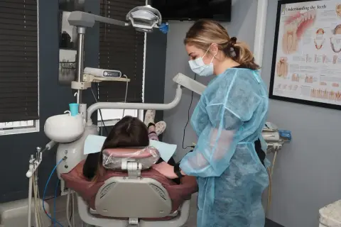 Dentystka w fartuchu przygotowuje się do skalingu i piaskowania NFZ. Pacjentka leży w fotelu.