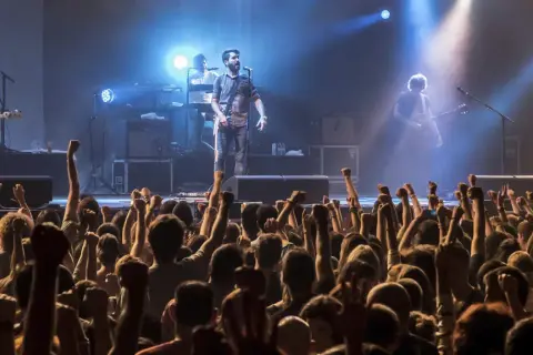 Una banda en vivo toca para una multitud eufórica. Los **fiz horarios** de la música llenan el aire mientras los fans levantan los puños.