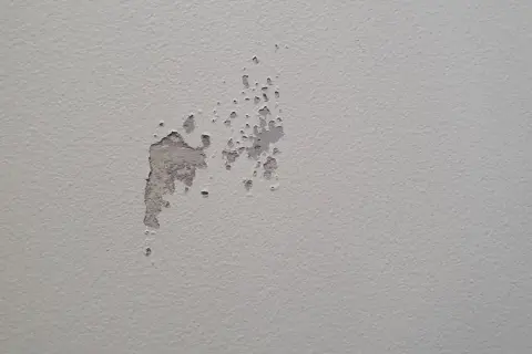 Sprucken färg visar spackel syns efter målning. En fläck på en ljusgrå vägg där färgen flagnar och spacklet syns igenom.