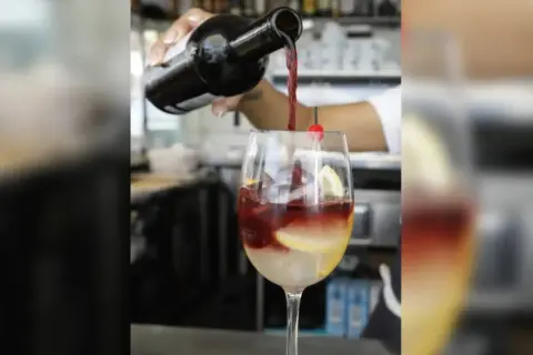 Rotwein wird in ein Glas mit Eis, Zitrone und Kirsche gegossen. Perfekt für rotwein im sommer.