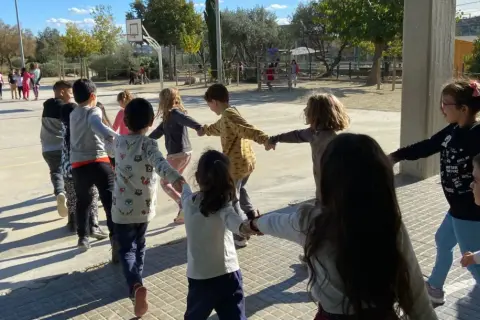 Niños jugando en círculo, tomados de la mano, en una actividad de juegos de conocimiento del medio al aire libre.