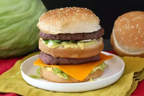 Burger double étage avec fromage, laitue et sauce sur une assiette blanche.