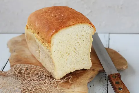 Świeżo upieczony chleb tostowy na desce, obok nóż do chleba. Idealny na śniadanie.