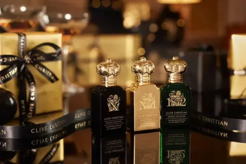 Trzy butelki najdroższych perfum Clive Christian w złotych opakowaniach, ozdobione czarną wstążką z logo marki.